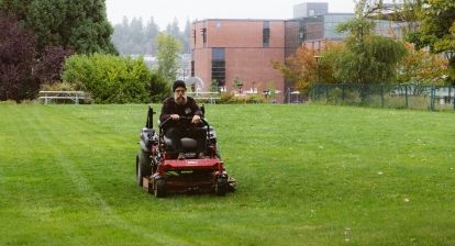 Groundskeeper mowing campus lawn on a riding lawnmower